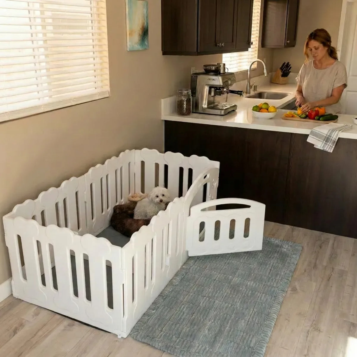 White pet gate in a kitchen with pets inside, woman preparing food in the background